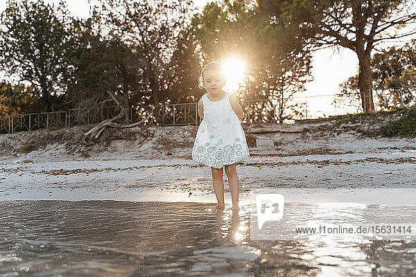 Süßes Kleinkind  das bei Sonnenuntergang am Strand steht