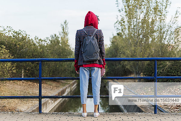 Rückenansicht einer jungen Frau mit Rucksack und Mobiltelefon auf einer Brücke stehend