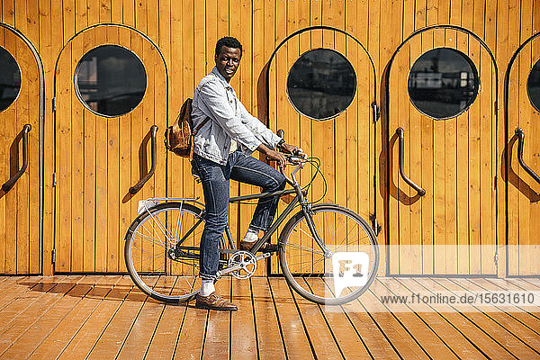 Junger Mann fährt Fahrrad vor Holztüren