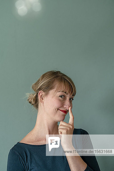 Porträt einer lächelnden Frau  die ihre Nasenspitze berührt