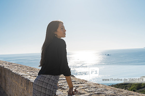Junge brünette Frau  die vom Aussichtspunkt auf Ibiza in die Ferne schaut