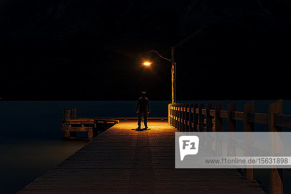 Rear view of a man standing on pier at night