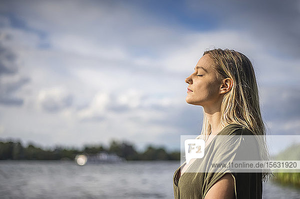 Frau mit geschlossenen Augen an einem See stehend