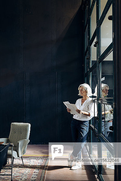 Beiläufige reife Geschäftsfrau beim Durchsehen von Papieren im Loft-Büro