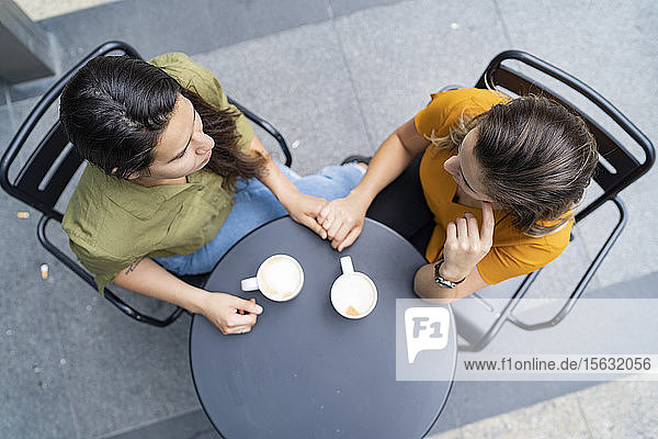 Draufsicht auf ein lesbisches Paar  das in einem Straßencafé Händchen hält