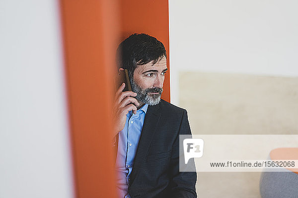 Reifer Geschäftsmann sitzt in einer Nische und telefoniert mit dem Handy