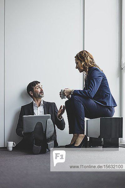 Geschäftsfrau mit einem Geschäftsmann im Büro  der auf dem Boden sitzt und einen Laptop benutzt