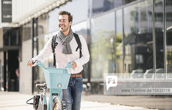 Lächelnder junger Mann mit Fahrrad in der Stadt unterwegs