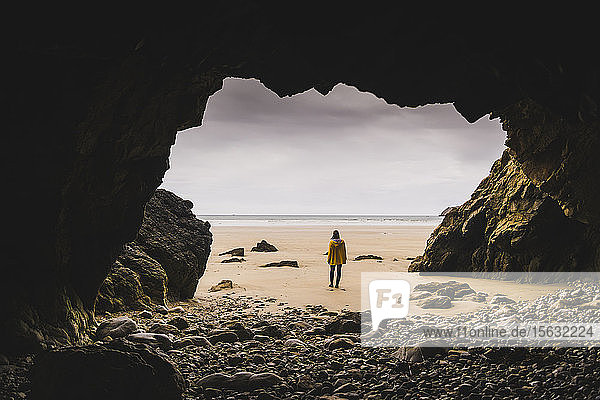 Junge Frau in gelber Regenjacke am Strand der Felshöhle  Bretagne  Frankreich