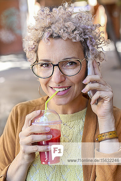 Portrait of a woman using smartphone and drinking a juice outdoors