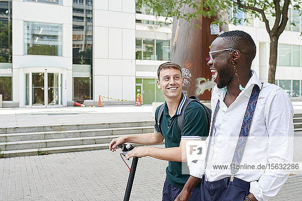 Zwei glückliche Geschäftsleute mit E-Scooter im Gespräch in der Stadt