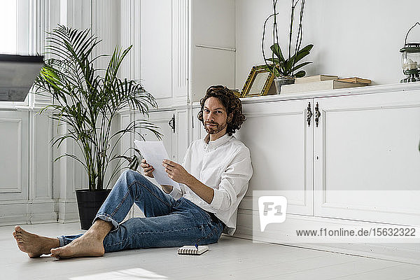 Porträt eines Mannes  der zu Hause auf dem Boden sitzt und Papiere durchsieht