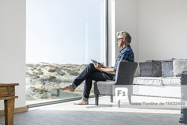 Lässiger Geschäftsmann sitzt in modernem Haus und benutzt Tablet