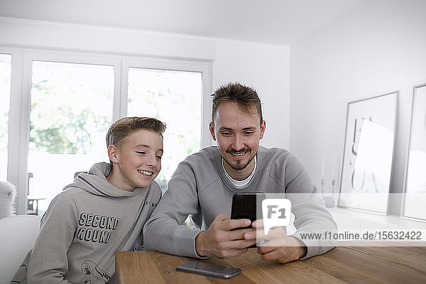 Junger Mann und Teenager benutzen ein Smartphone im Wohnzimmer