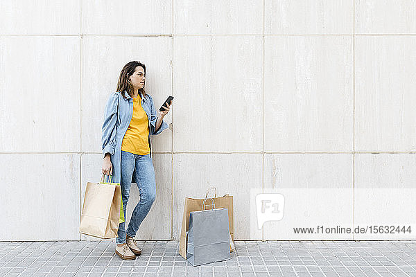 Junge brünette Frau benutzt Smartphone nach dem Einkauf