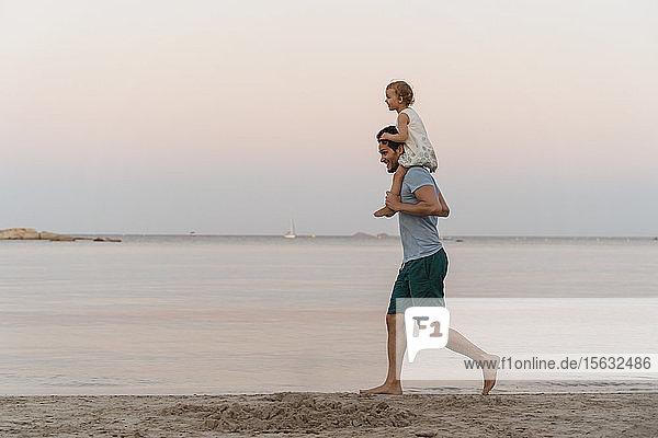 Happy father carrying daughter on shoulders on the beach at sunset
