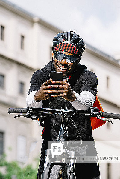 Stilvoller junger Mann mit Fahrrad  Smartphone und Kuriertasche in der Stadt