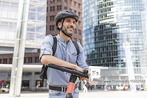 Smiling man with e-scooter on city square  Berlin  Germany