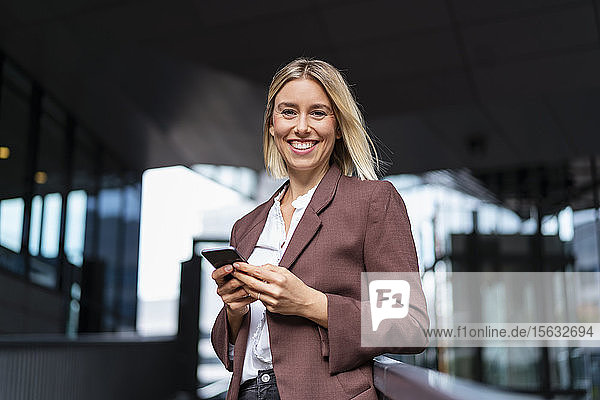 Portrait of happy young businesswoman with mobile phone in the city