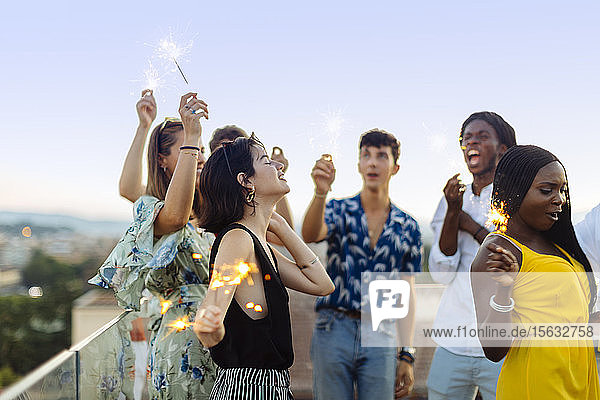 Gruppe glücklicher multiethnischer Freunde feiert am Abend eine Party mit Wunderkerzen