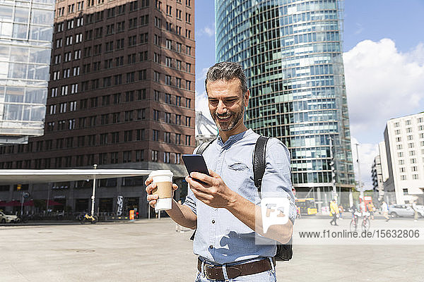 Lächelnder Geschäftsmann beim Blick auf das Smartphone in der Stadt  Berlin  Deutschland