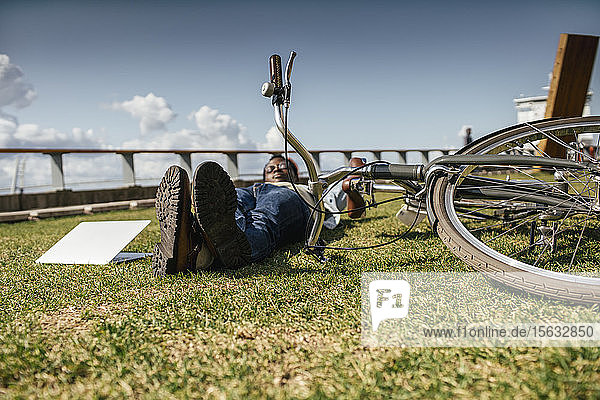Junger Mann mit Fahrrad  entspannend  im Gras liegend