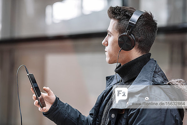 Junger Mann mit Smartphone und Kopfhörern beim Musikhören
