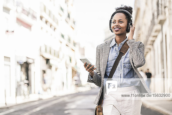 Smiling young woman with headphones and mobile phone in the city on the go  Lisbon  Portugal