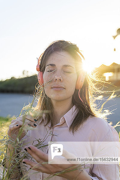 Porträt einer jungen Frau mit geschlossenen Augen  die in der Natur mit Kopfhörern Musik hört