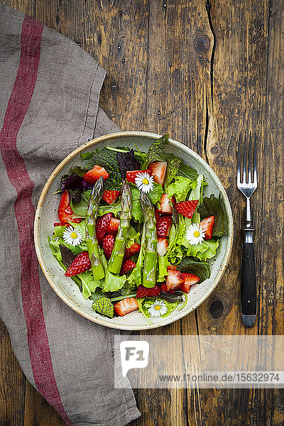 Nahaufnahme von Salat mit grünem Spargel Erdbeeren und Gänseblümchen
