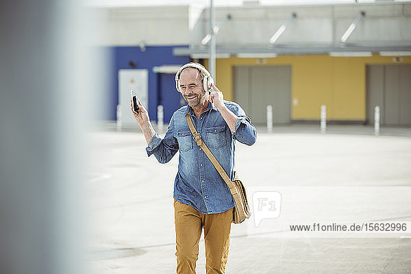 Glücklicher lässiger  reifer Mann mit Kopfhörern und Smartphone auf dem Parkdeck