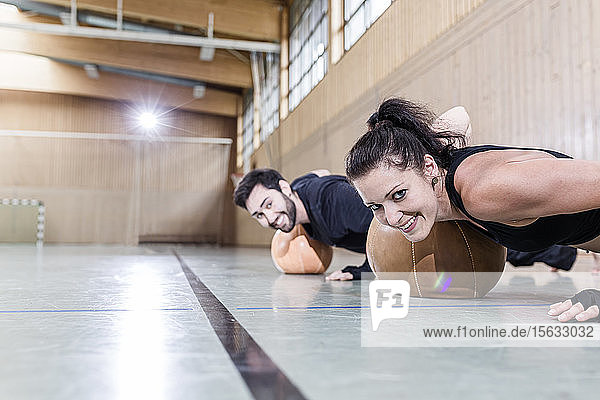 Man and smiling woman practising with medicine balls in sports hall