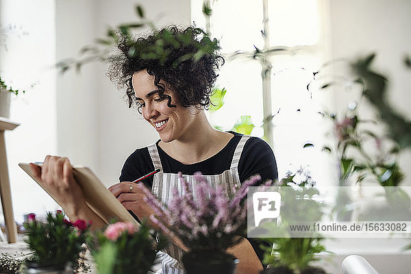 Lächelnde junge Frau mit Klemmbrett in einem kleinen Laden mit Pflanzen