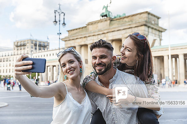 Porträt von drei Freunden  die sich mit dem Handy vor dem Brandenburger Tor in Berlin selbstständig machen