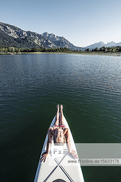 Girl sitting on SUP board and looking at camera  from above  Lake Bannwaldsee  Germany