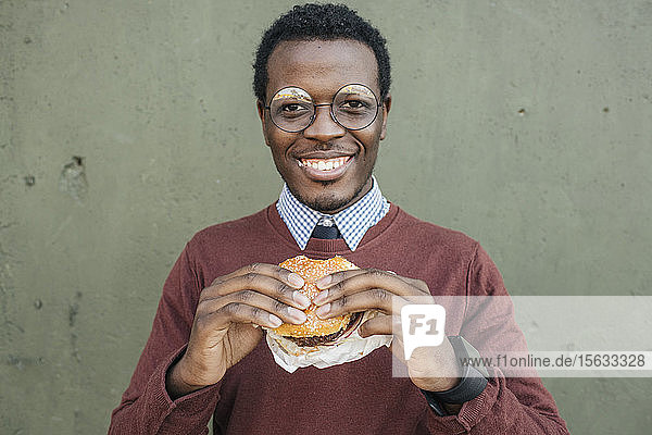 Junger Mann isst Cheeseburger und lächelt