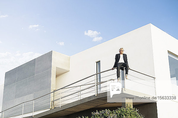 Geschäftsmann sitzt auf einem Geländer vor seinem modernen Haus