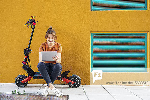 Porträt einer Frau  die auf einem Elektroroller sitzt und ein digitales Tablet benutzt