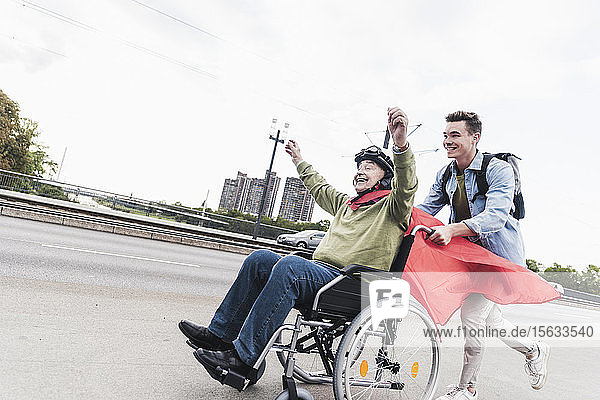 Young man pushing senior man sitting in a wheelchair dressed up as superhero