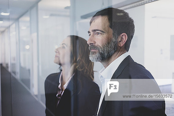 Portrait of businesswoman and businessman in office looking through glass pane