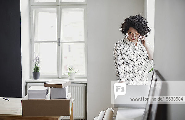 Lächelnde junge Frau am Telefon mit Laptop im Home-Office
