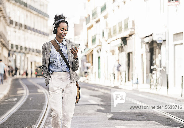 Smiling young woman with headphones and mobile phone in the city on the go  Lisbon  Portugal