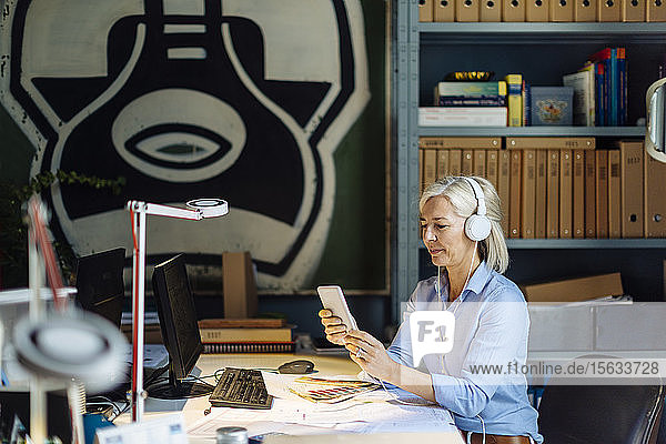 Reife Frau  die mit Kopfhörern telefoniert und im Architekturbüro sitzt