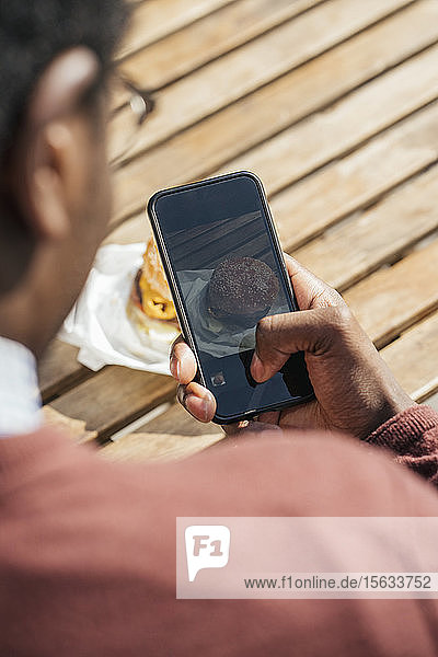 Junger Mann fotografiert seinen Cheeseburger mit seinem Smartphone
