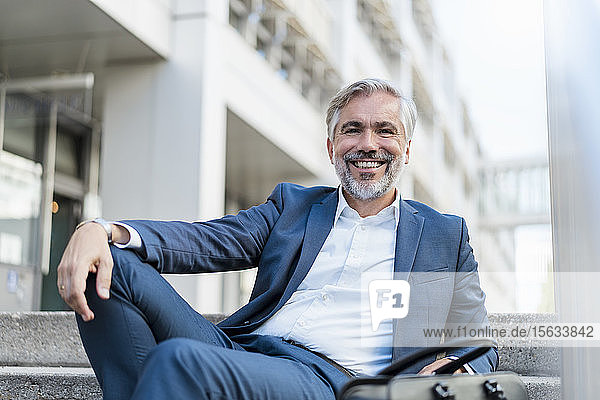 Portrait of smiling mature businessman sitting on stairs in the city