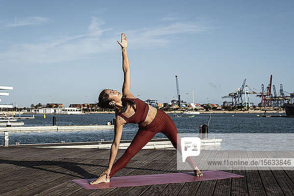 Asiatische Frau beim Yoga am Hafen  Dreieckshaltung