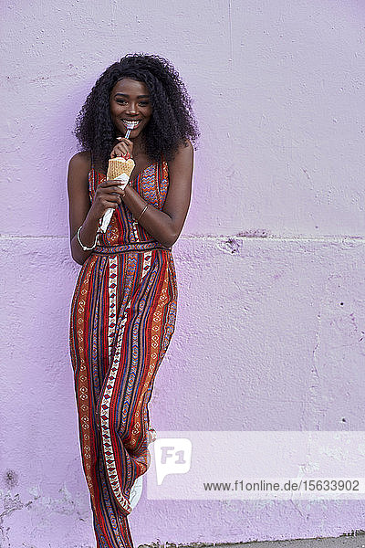 Porträt einer jungen Frau  die vor einer violetten Wand Eis isst