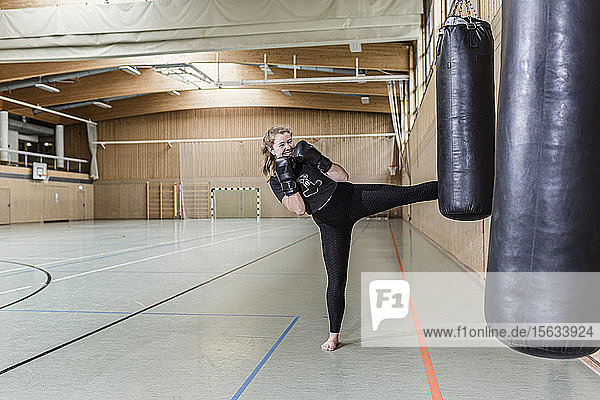 Female kickboxer practising at punchbag in sports hall