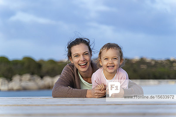 Porträt einer glücklichen Mutter und Tochter  die bei Sonnenuntergang auf einem Steg liegen