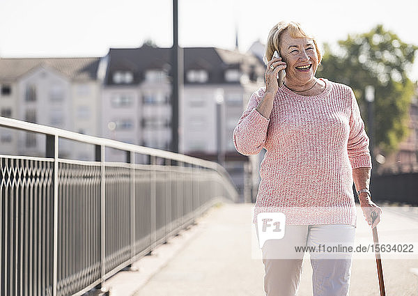 Ältere Frau  die auf einer Fußgängerbrücke geht  Gehstock benutzt und telefoniert
